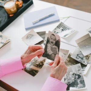 A person in a pink shirt organizing old black and white family photos on a table.